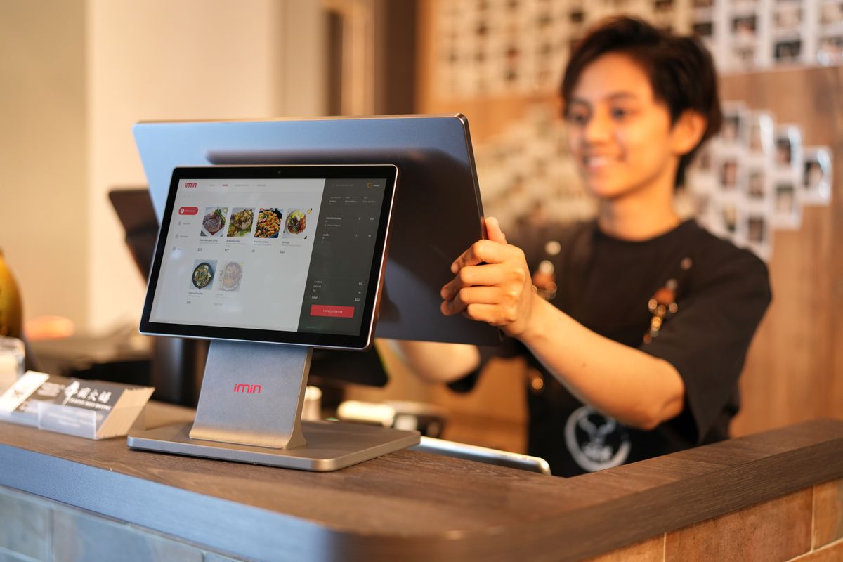 Cajero sonriente registrando una venta en un punto de venta con pantalla táctil